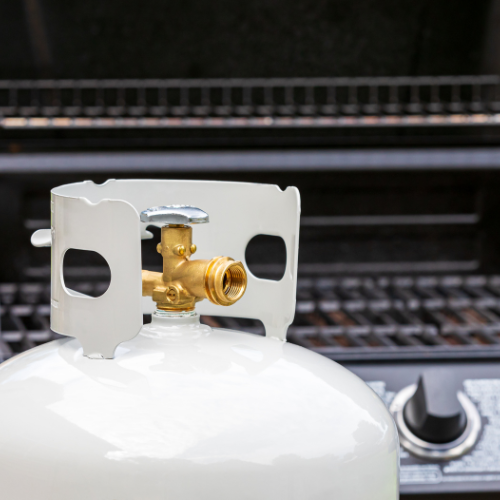 A propane tank in front of a propane grill.